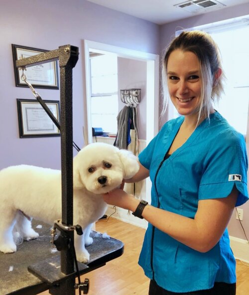 Josie Belmont smiling while grooming a freshly trimmed white bichon on her grooming table